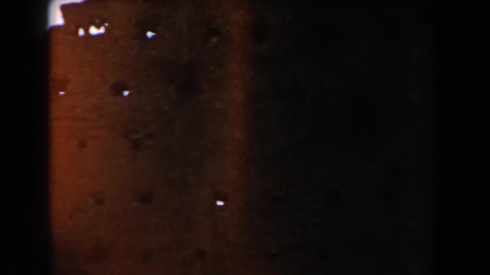 Underexposed 8mm frame from the Casablanca clip showing a reddish masonry surface, dark edges, and visible film specks.