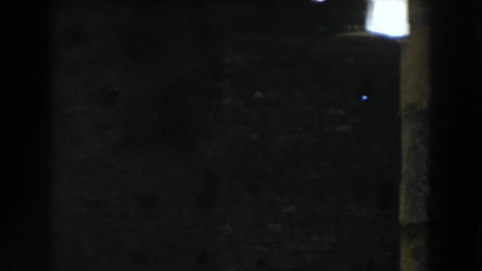 Dark 1959 Casablanca-area 8mm frame with a partial column at right, grass below, and heavy shadow across the ruins.