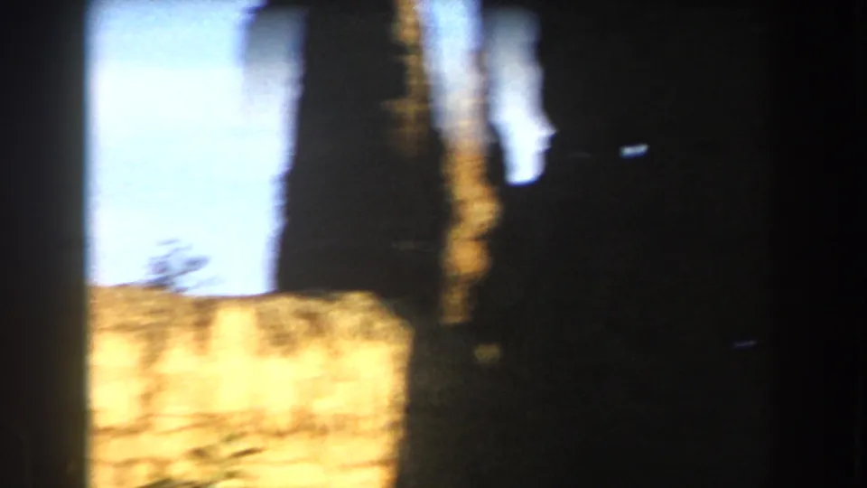 Blurred final 8mm frame showing bright sky, a stone or masonry surface, dark edges, and strong light leaks or film wear.