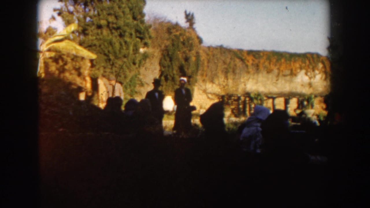 People in a shaded garden near stone walls and greenery.