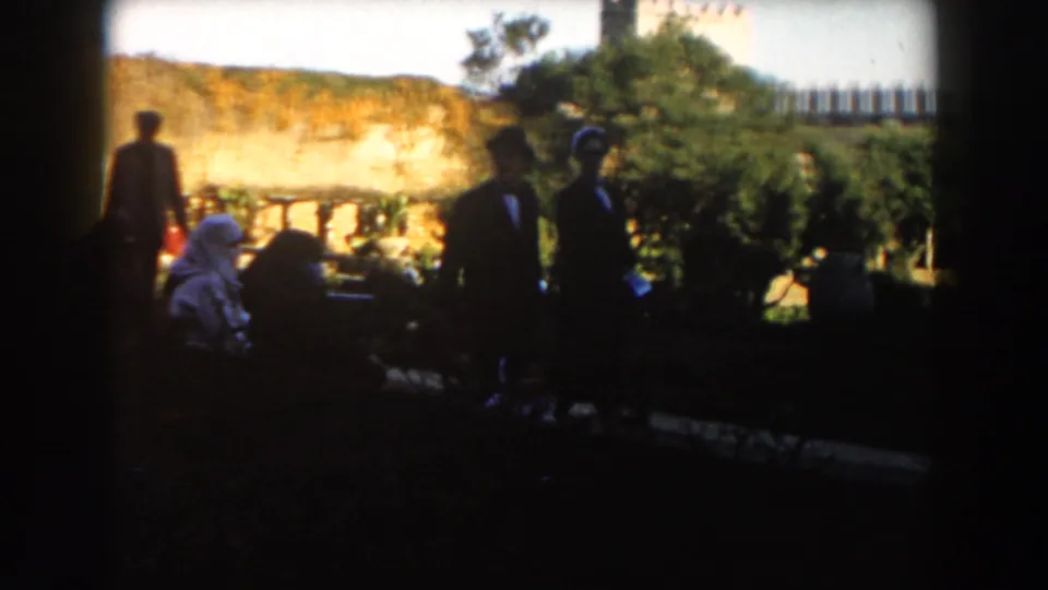 Two elegant adults walk through a Casablanca garden as other visitors sit or stand nearby.