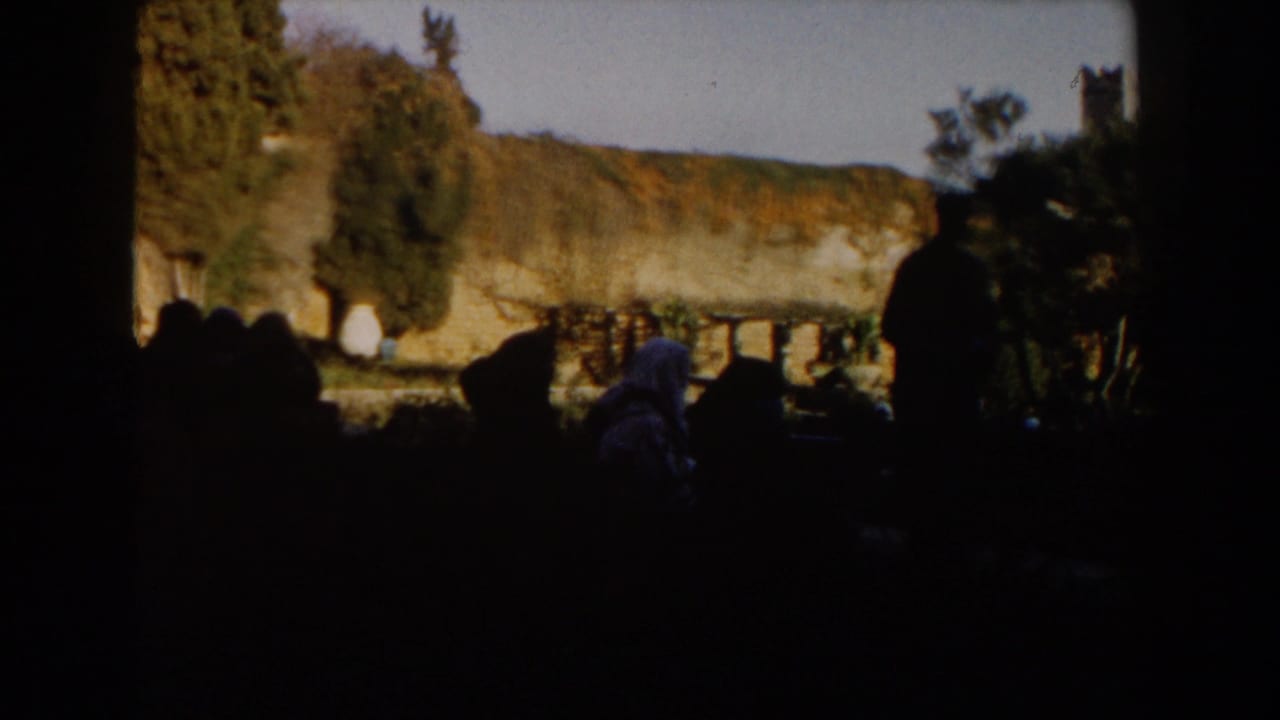 1959 Casablanca home-movie frame showing dark foreground figures before a sunlit vine-covered wall and trees.