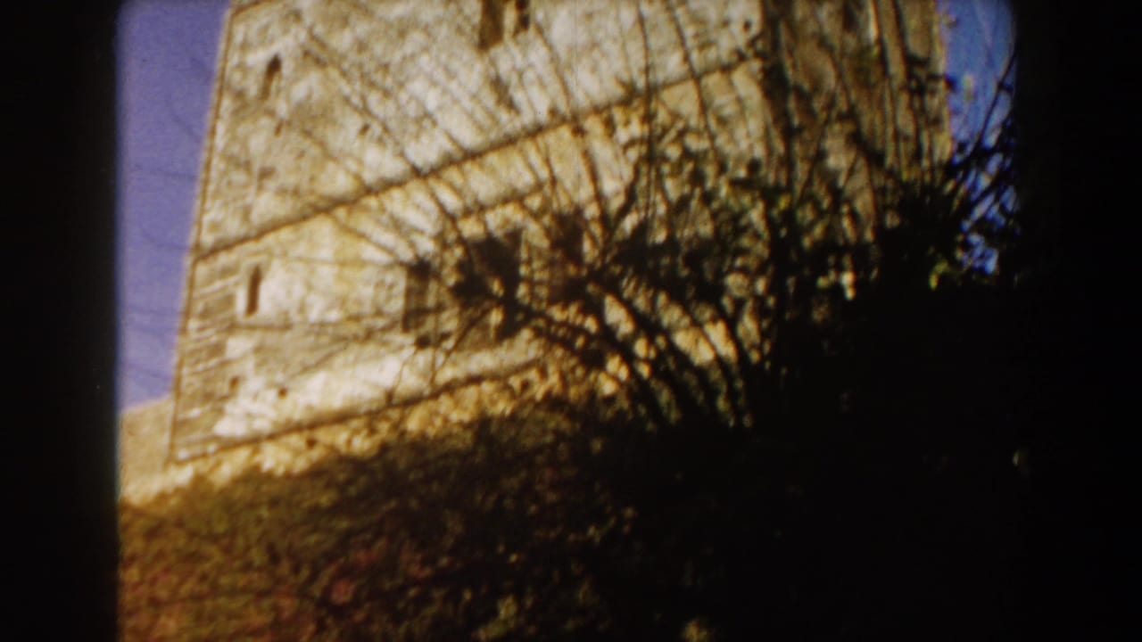 1959 Casablanca home-movie frame showing a weathered stone tower partly obscured by silhouetted vegetation.