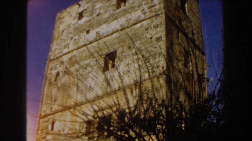 1959 Casablanca frame with a tall weathered stone tower, small window openings, and vegetation crossing the lower foreground.
