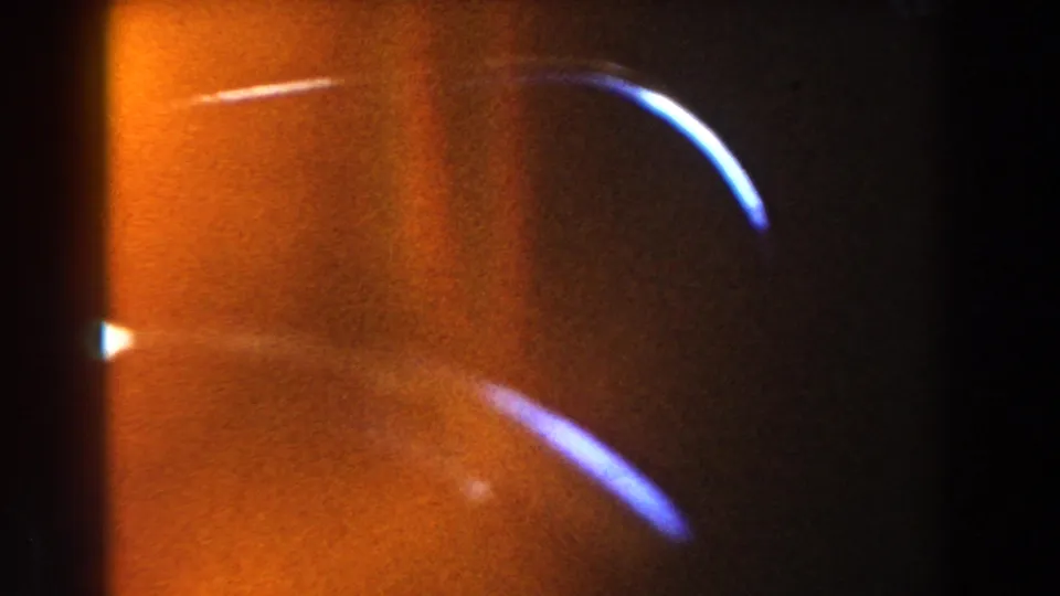 End-frame 8mm artifact showing warm orange exposure flare and curved blue-white light streaks rather than a clear architectural view.