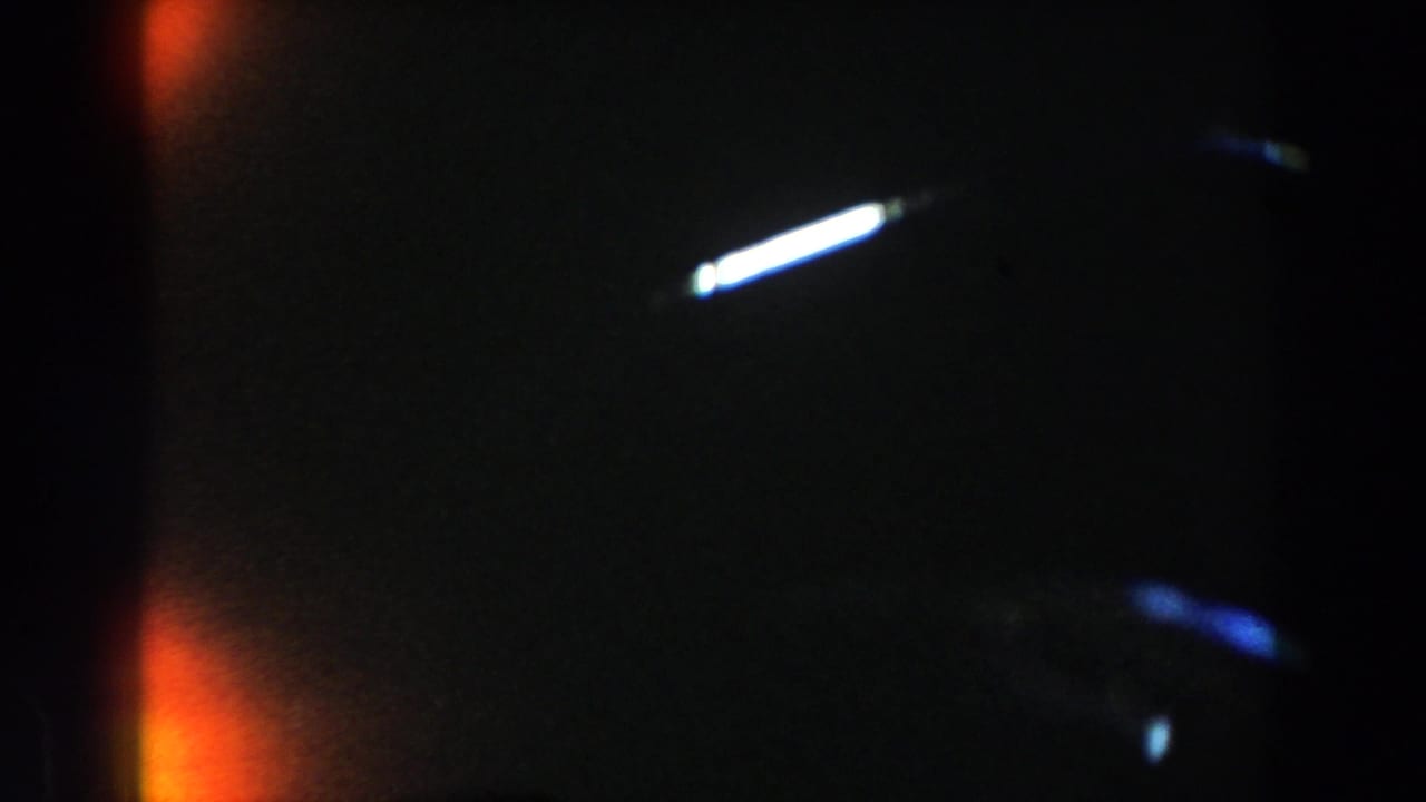 1959 Casablanca 8mm artifact frame with dark exposure, orange light leak, white flare streak, blue streaking, and visible film grain.