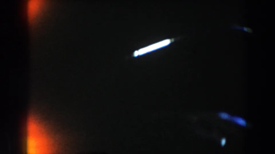 1959 Casablanca 8mm artifact frame with dark exposure, orange light leak, white flare streak, blue streaking, and visible film grain.