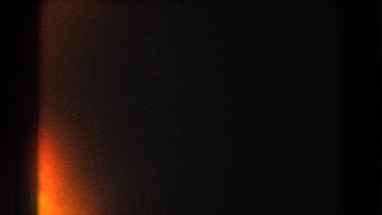 Dark frame with broad orange flare at the left edge and faint grain across the film.