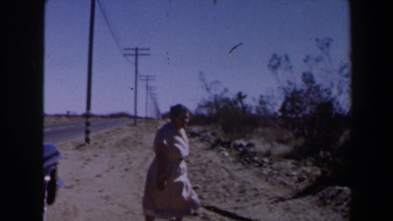 In 1958 Las Vegas-area home-movie footage, a woman walks along a sandy roadside under utility lines in a sparse desert landscape.