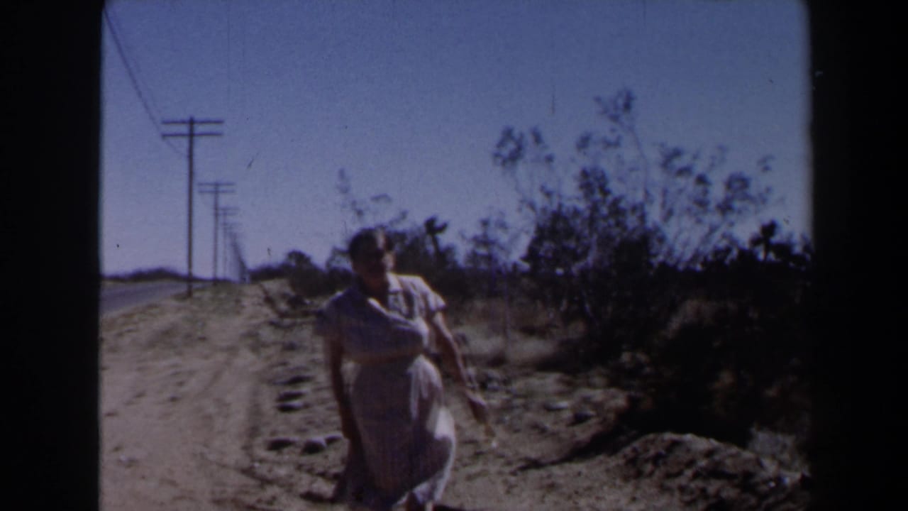 Woman nearing the camera on a dirt roadside with desert brush and power lines in the background.