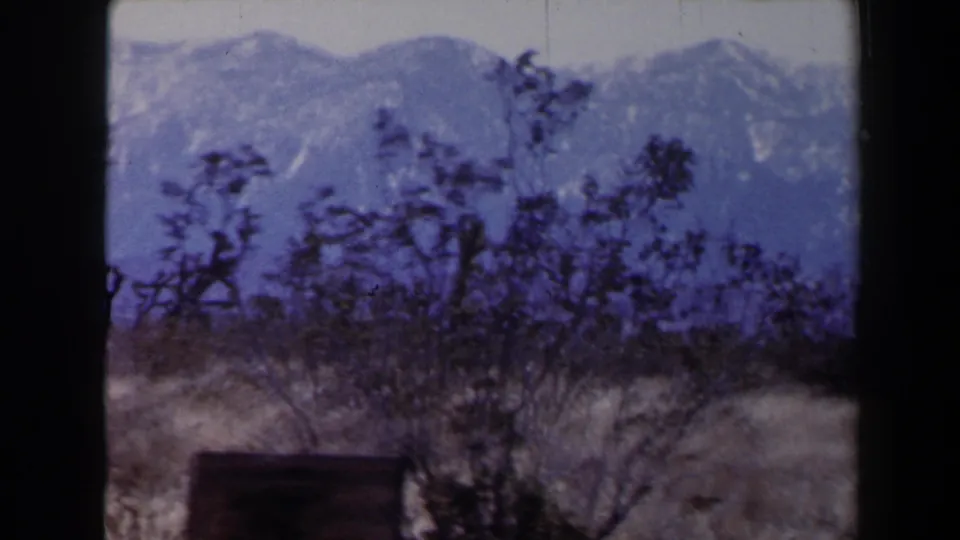 1958 8mm Las Vegas-area view of snow-dusted mountains behind sparse desert brush and dry foreground grass.