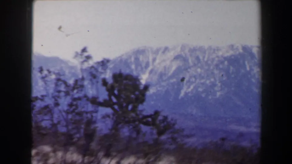 Las Vegas-area 8mm landscape frame showing snow-streaked mountains behind dark desert shrubs and a pale sky.