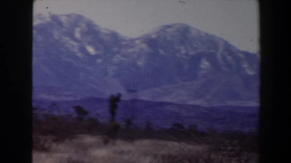Vintage 8mm frame of a broad snow-marked mountain slope above open desert terrain near Las Vegas.