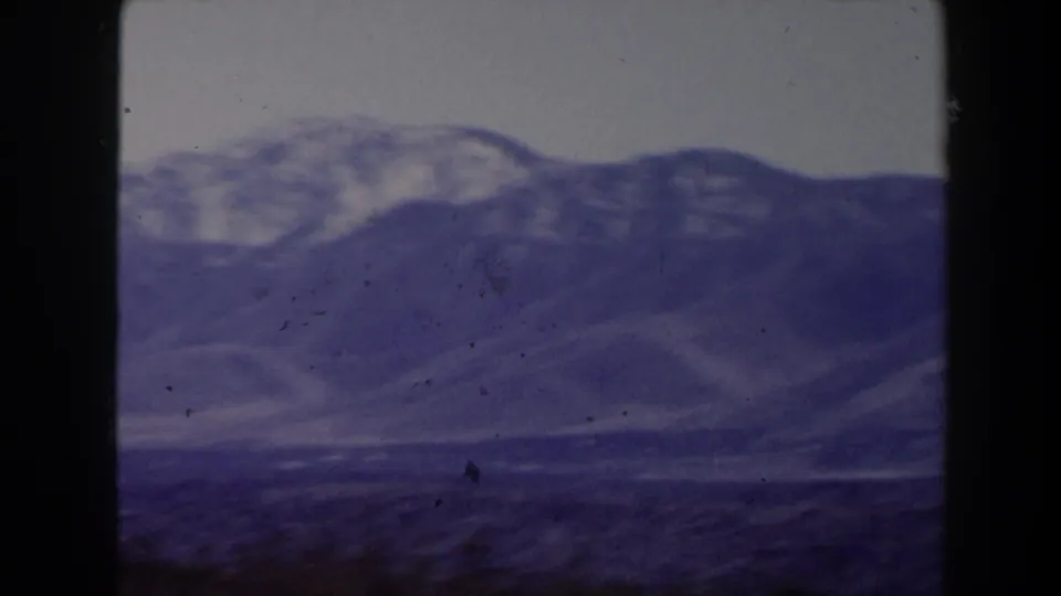 1958 8mm frame likely near Las Vegas showing hazy blue-purple desert mountain ridges under a pale sky.