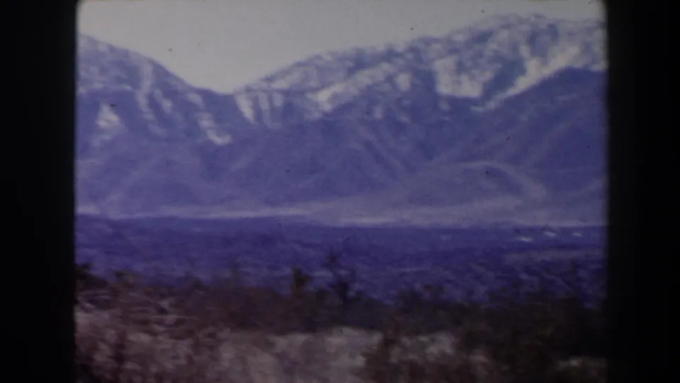 1958 8mm view near Las Vegas of a broad, hazy mountain slope with snow traces and sparse foreground scrub.