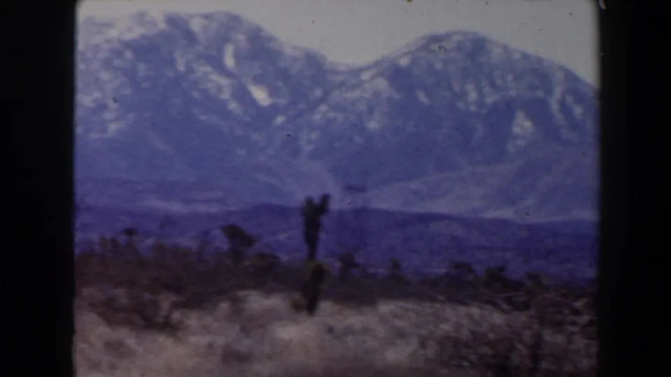 Likely Las Vegas-area 1958 frame showing snow-dusted mountains and a silhouetted desert plant in the foreground.
