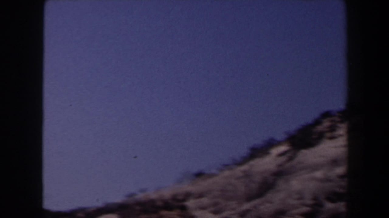 Faded 1958 Las Vegas-area desert frame showing a rocky slope beneath broad blue sky.