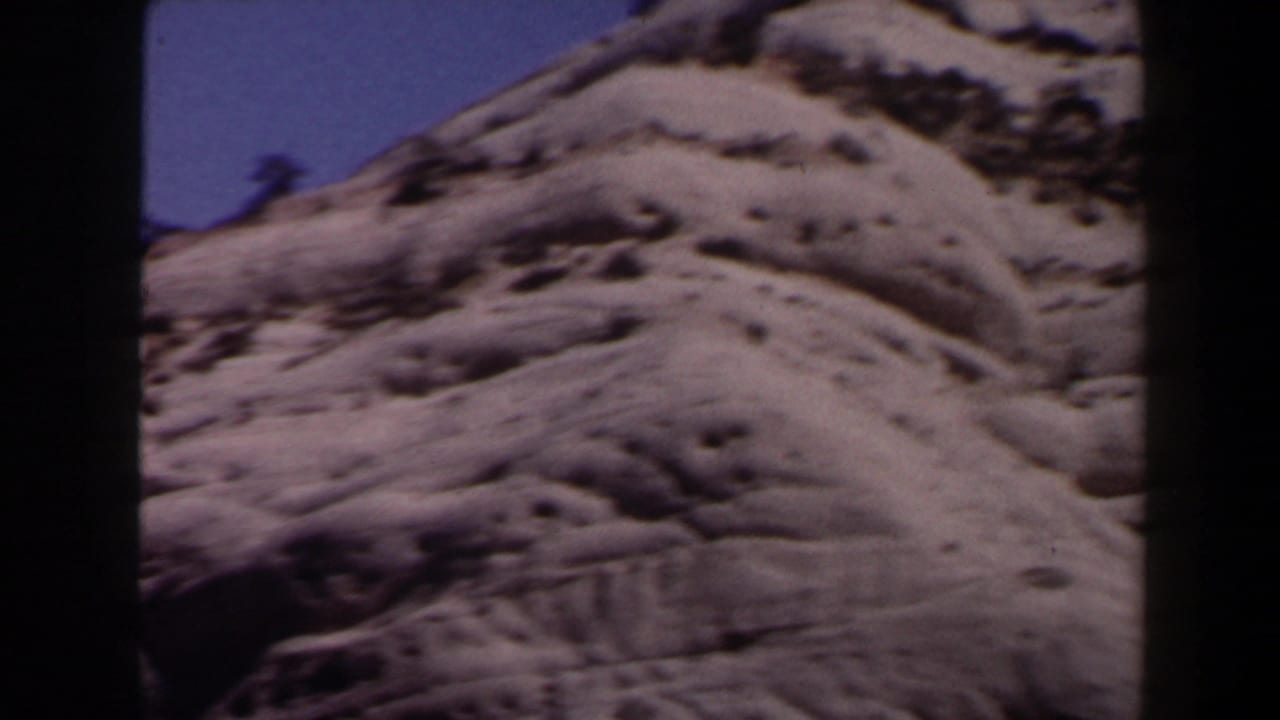 1958 Las Vegas-area desert hillside with pale rock, sparse scrub, and 8mm frame borders.