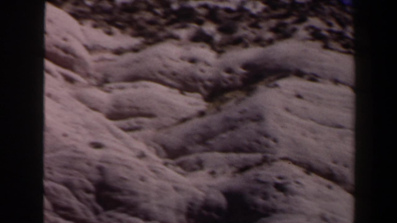 Sandy desert hillside with dark scrub patches and 8mm frame borders.