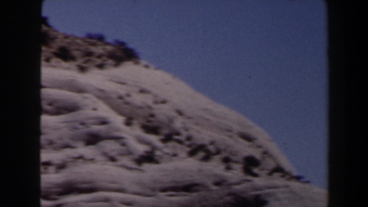 A pale sandy hill near Las Vegas in 1958, with scattered dark vegetation and blue sky along the upper edge.