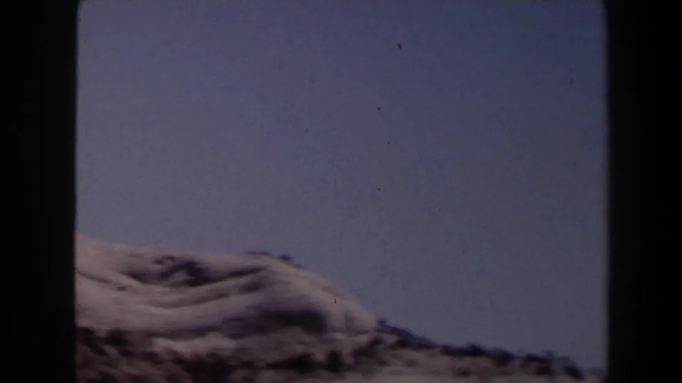 Final 1958 Las Vegas-area frame with a low sandy ridge, sparse scrub, and broad blue sky from a moving home-movie shot.