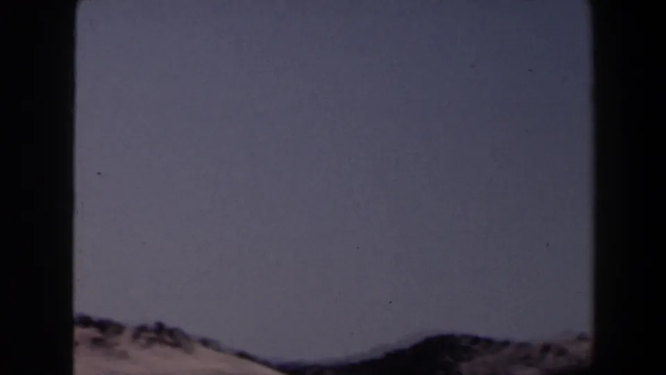 1958 8mm Las Vegas-area landscape frame with pale sky and distant dark ridges partly obscured by film gate shadow.