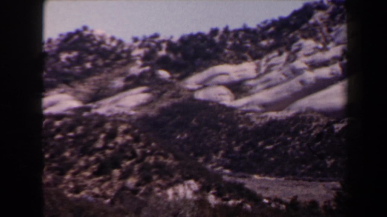 Snowy rocky mountain slope near Las Vegas in 1958 home-movie footage, with sparse evergreens and a clear sky.