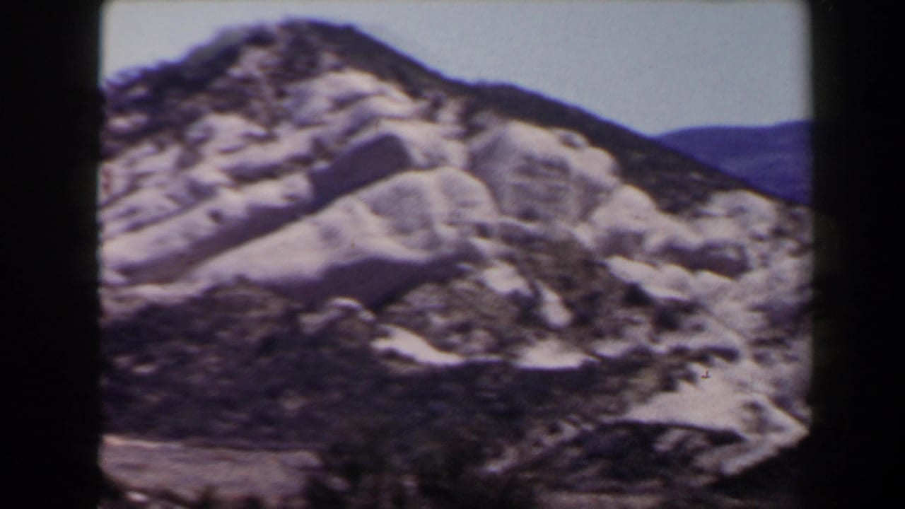 Handheld 8mm view of a snow-covered Las Vegas-area hillside, with exposed rocks and muted blue ridges beyond.