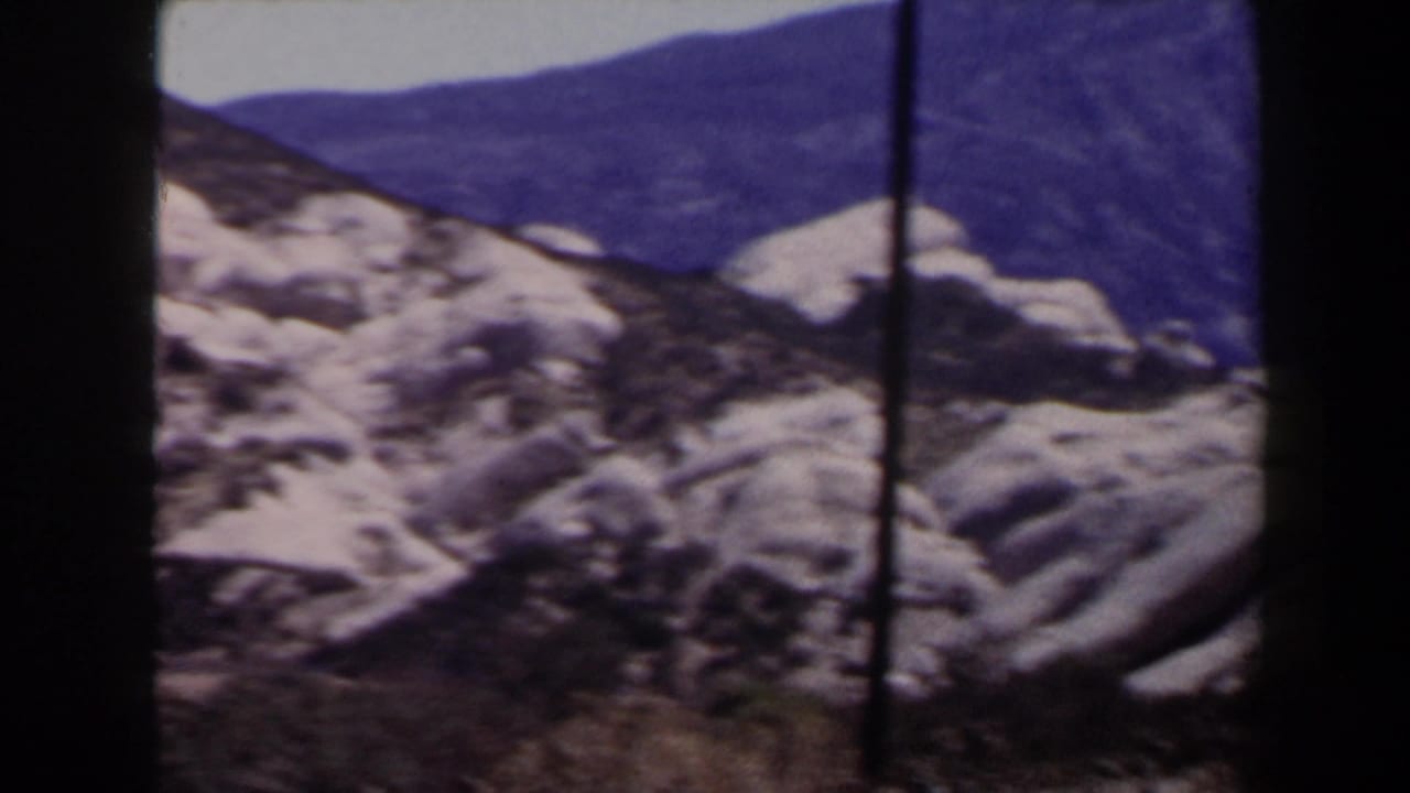 1958 8mm Las Vegas-area mountain view with snow-covered rocks, distant ridges, and a vertical brown pole in front.