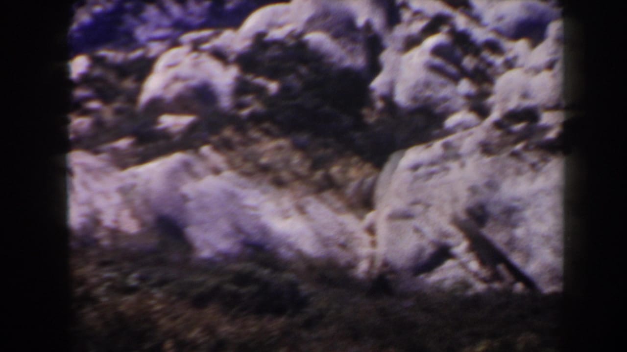 1958 Las Vegas-area 8mm frame showing rounded desert boulders, dry ground, and scrub with soft focus and visible film grain.