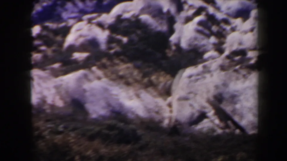 1958 Las Vegas-area 8mm frame showing rounded desert boulders, dry ground, and scrub with soft focus and visible film grain.