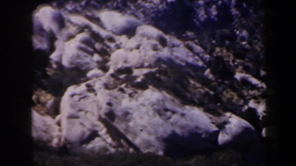1958 Las Vegas-area 8mm frame with large pale desert boulders, dark brush, and pronounced frame-edge shadow from the scanned film.