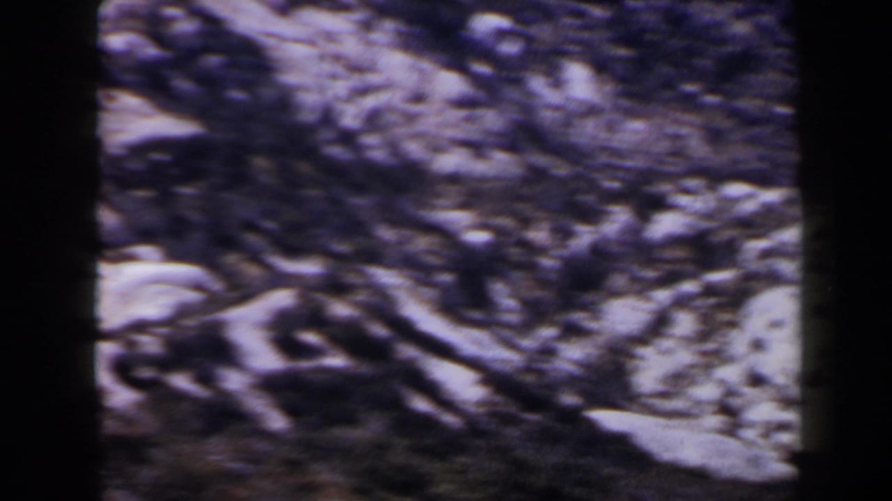 1958 Las Vegas-area frame with motion-softened rocky ground, pale stones, and dark foreground texture from the handheld pan.