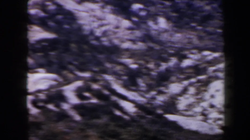 1958 Las Vegas-area frame with motion-softened rocky ground, pale stones, and dark foreground texture from the handheld pan.