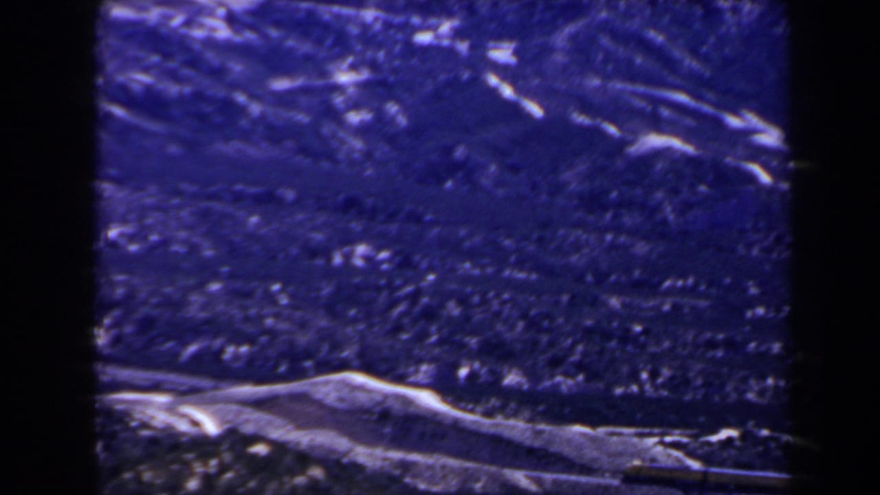 Purple-blue 8mm frame showing distant ridges and rough mountain terrain, with snow visible near the bottom edge.