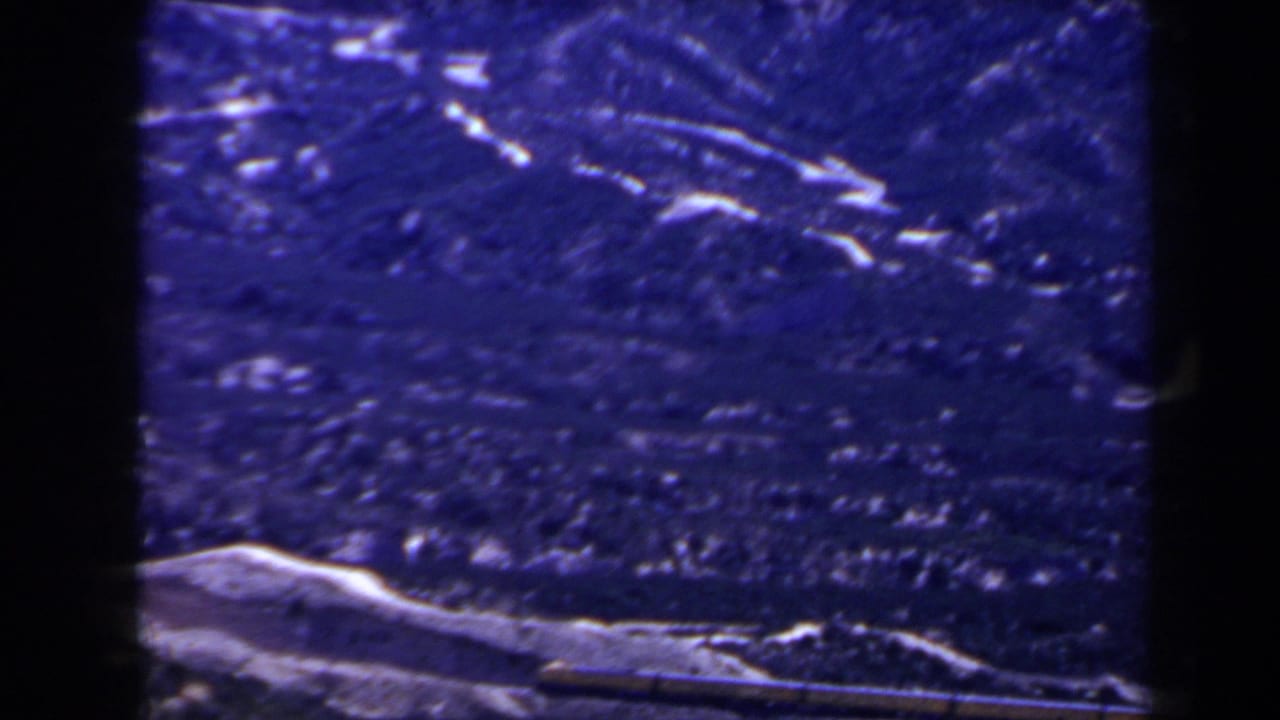 1958 home-movie frame of mountain ridges near Las Vegas, with a low snow patch and visible grain in a blue-shifted scan.