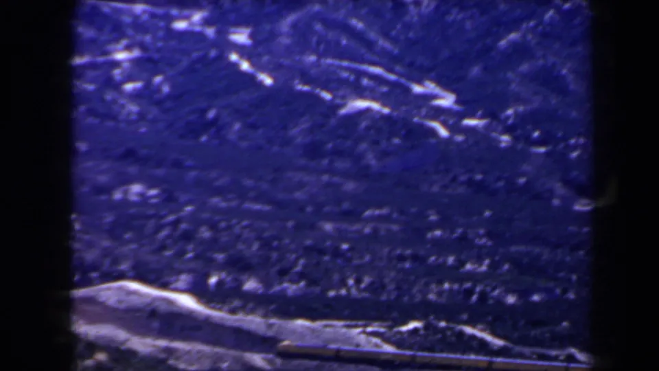 1958 home-movie frame of mountain ridges near Las Vegas, with a low snow patch and visible grain in a blue-shifted scan.