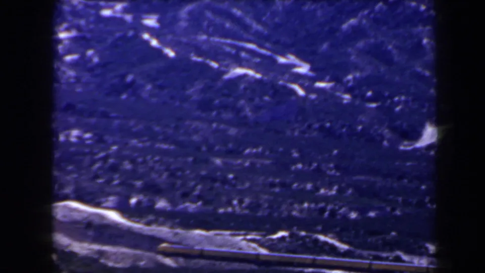 1958 8mm frame showing a blue-tinted snow-covered mountain slope above a darker lower landscape, with visible film edges.