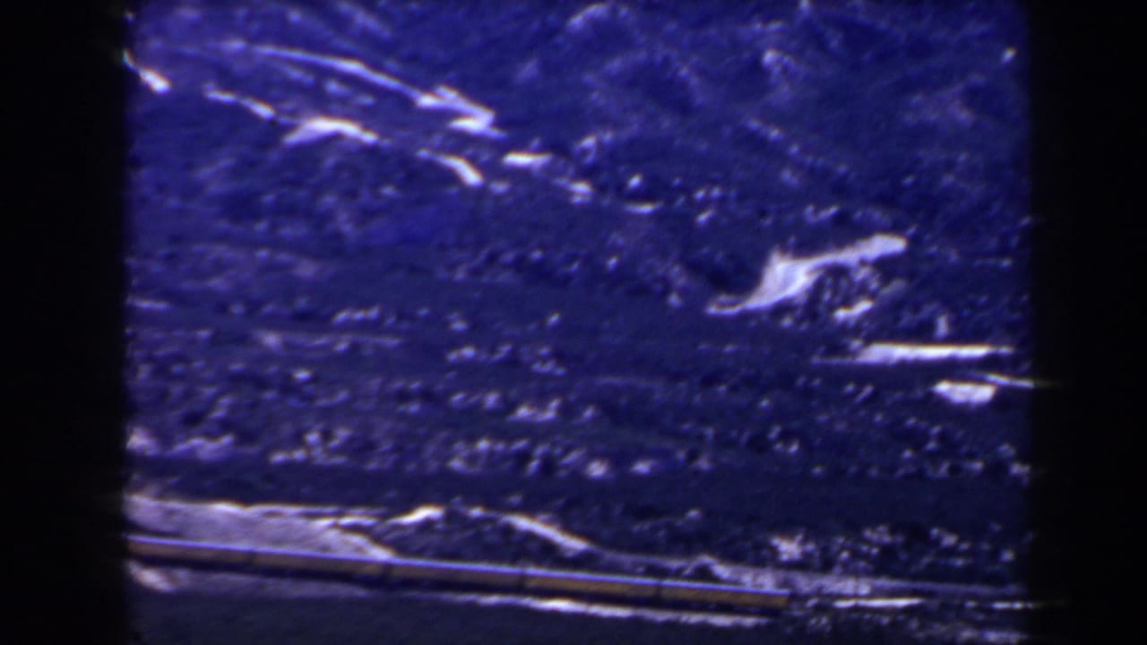 1958 8mm frame of distant snow-streaked mountain terrain near the supplied Las Vegas context, with a narrow possible rail or train line below.