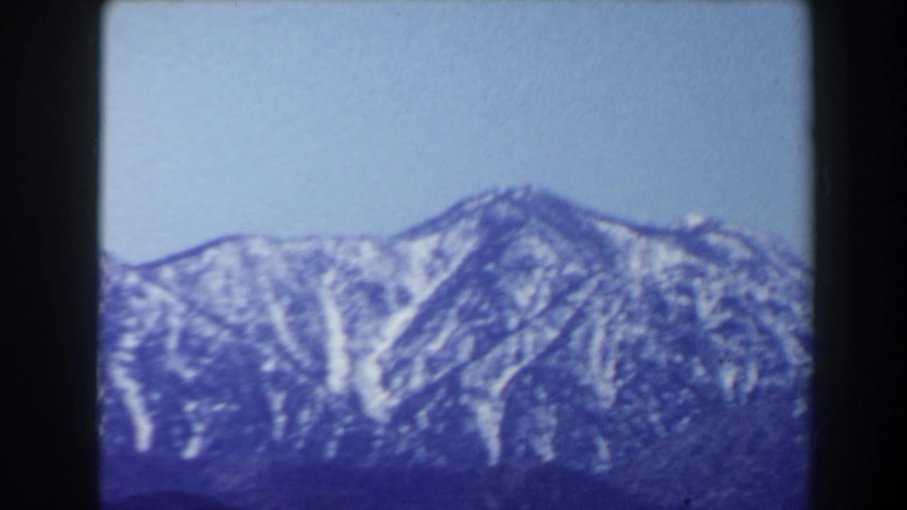 Wider 1958 8mm frame of snow-capped mountain peaks under a pale sky, consistent with the supplied Las Vegas travel metadata.
