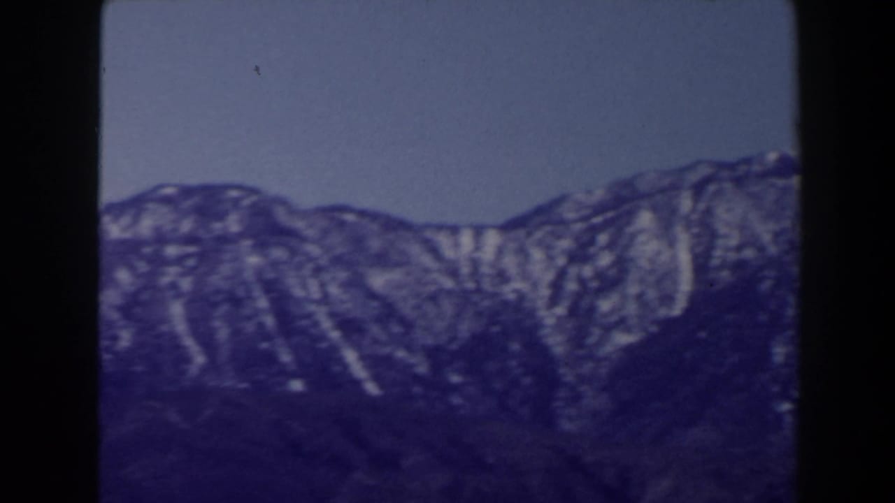 1958 Las Vegas-area 8mm view of a rugged mountain range with vertical snow patches and a clear sky above.