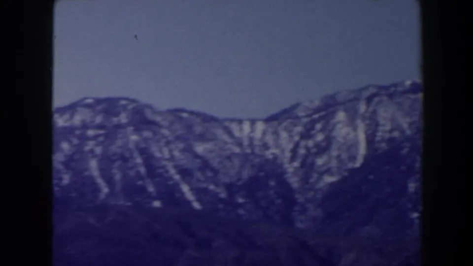 1958 Las Vegas-area 8mm view of a rugged mountain range with vertical snow patches and a clear sky above.