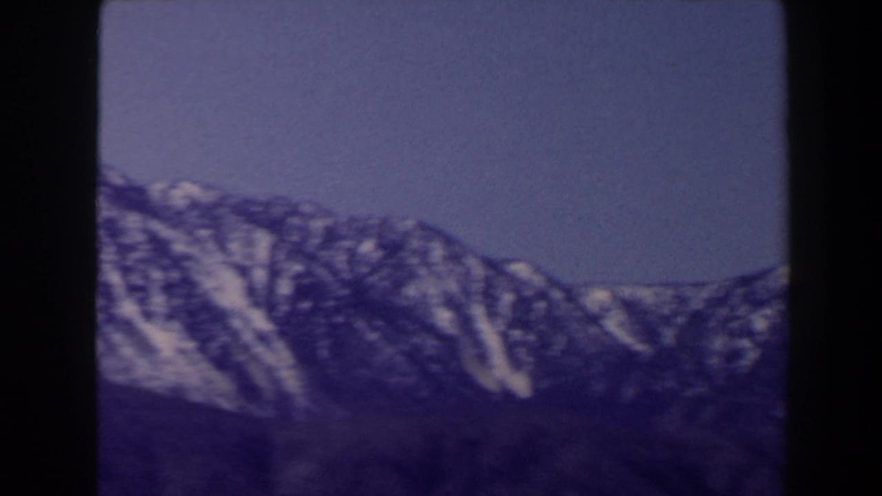 1958 Las Vegas-area travel footage frame with snow-lined slopes, dark foreground terrain, and a strong blue-purple 8mm cast.