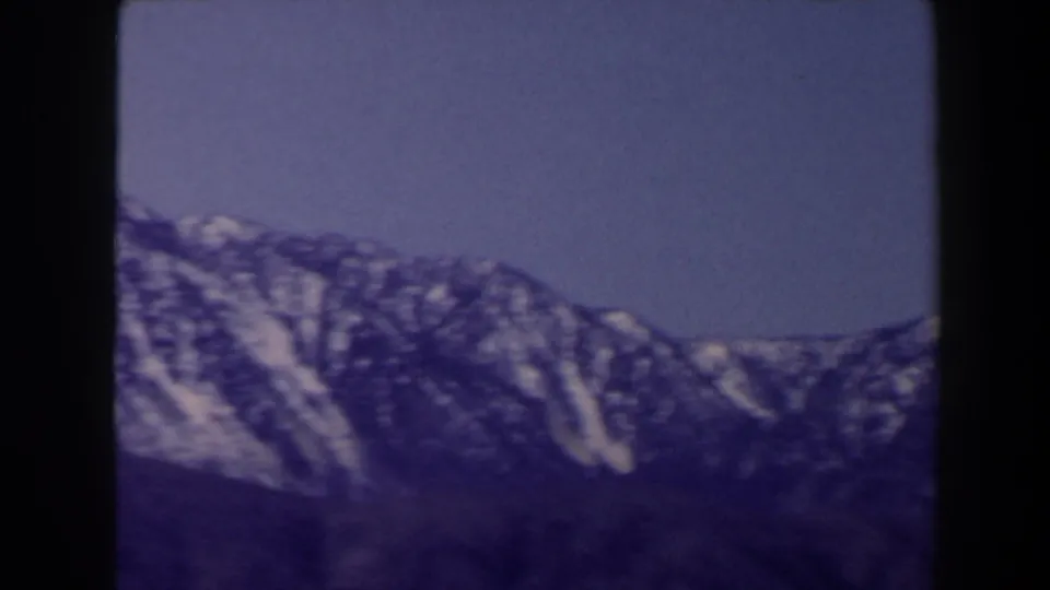 1958 Las Vegas-area travel footage frame with snow-lined slopes, dark foreground terrain, and a strong blue-purple 8mm cast.
