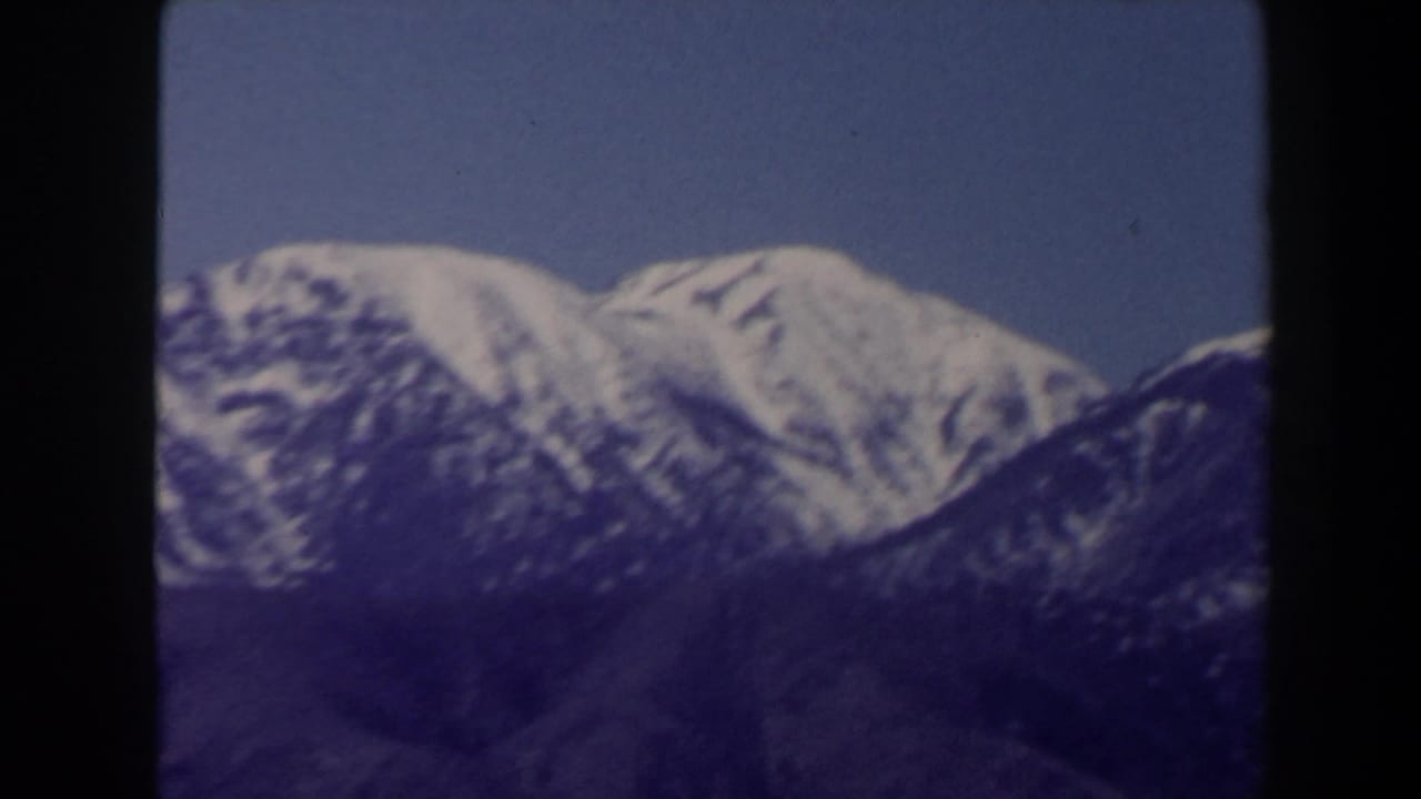 1958 Las Vegas-area 8mm frame showing a bright snow-capped peak against darker surrounding slopes and blue sky.
