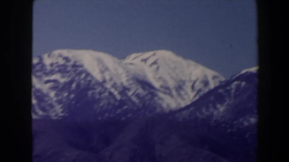 1958 Las Vegas-area 8mm frame showing a bright snow-capped peak against darker surrounding slopes and blue sky.
