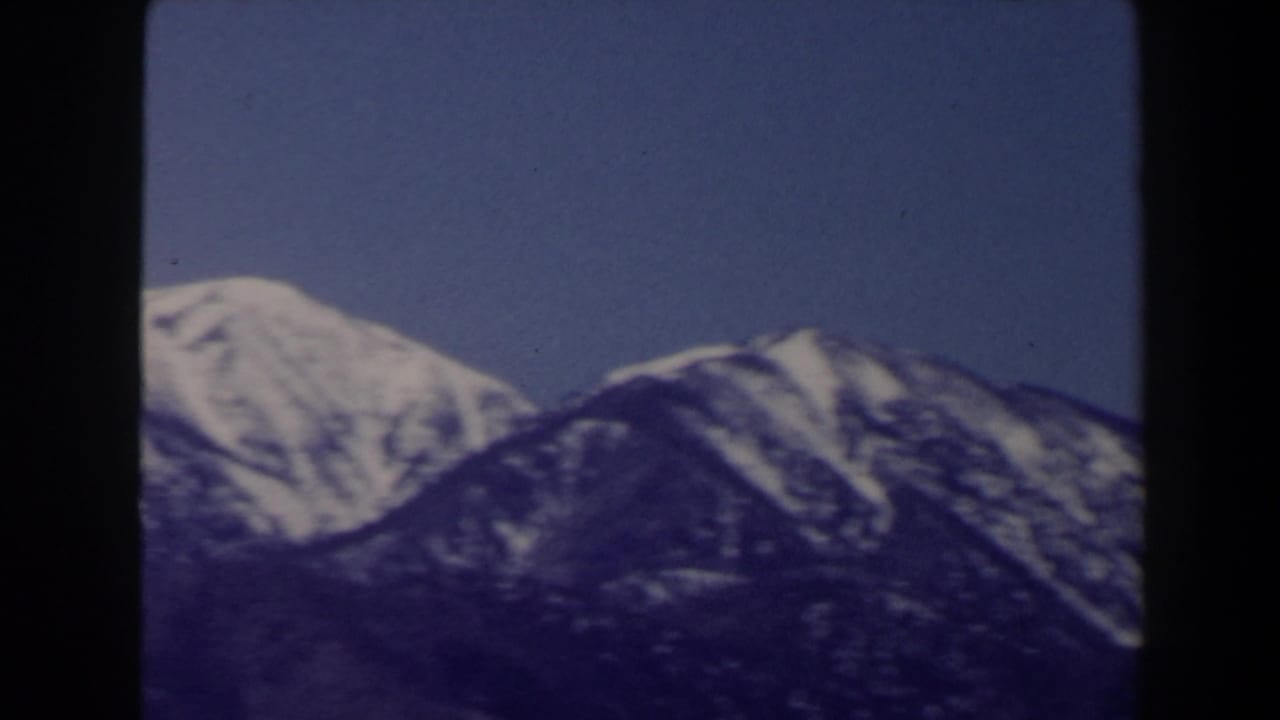 1958 8mm home-movie frame showing snow-dusted mountain peaks near Las Vegas under a clear blue sky.