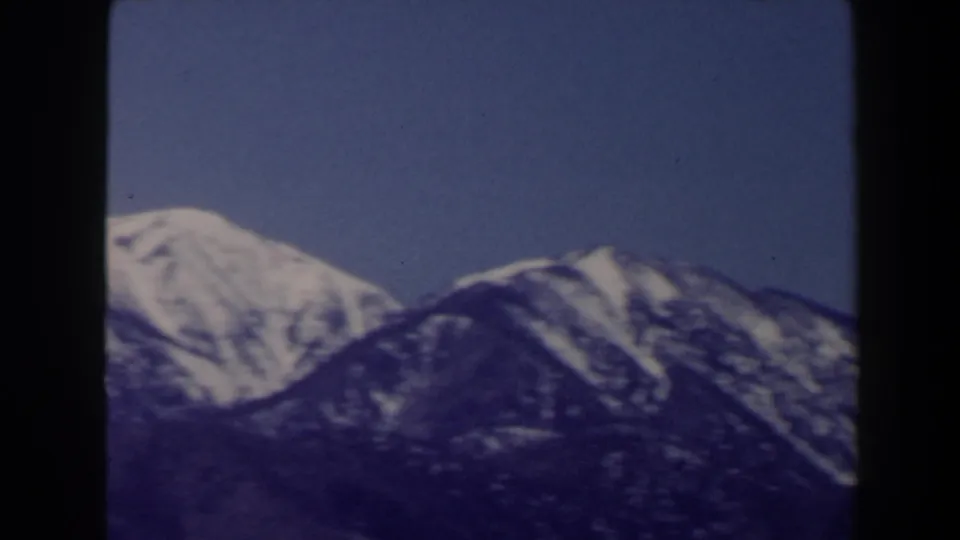 1958 8mm home-movie frame showing snow-dusted mountain peaks near Las Vegas under a clear blue sky.