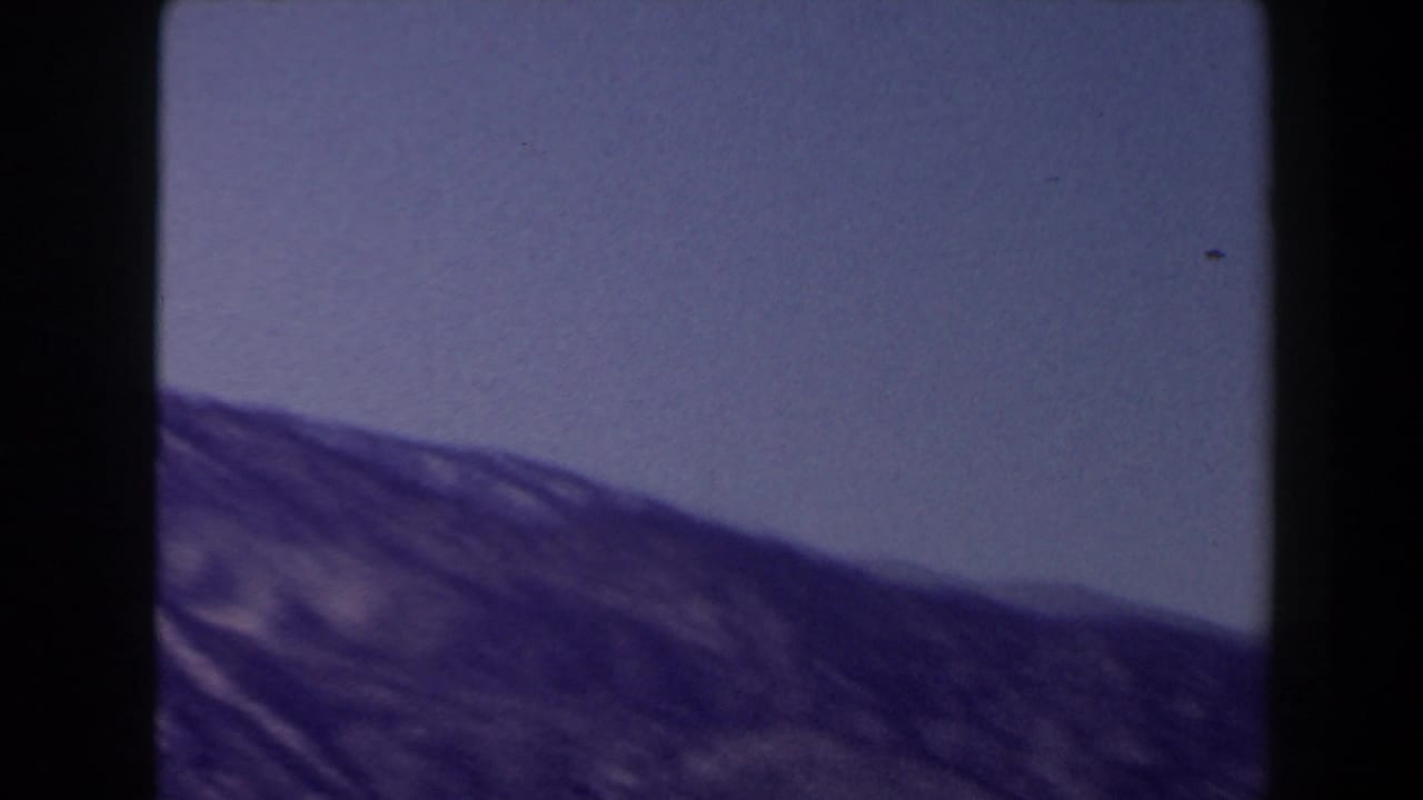 Soft 8mm frame of sloping mountain terrain and open blue sky, part of a 1958 Las Vegas-area home movie.