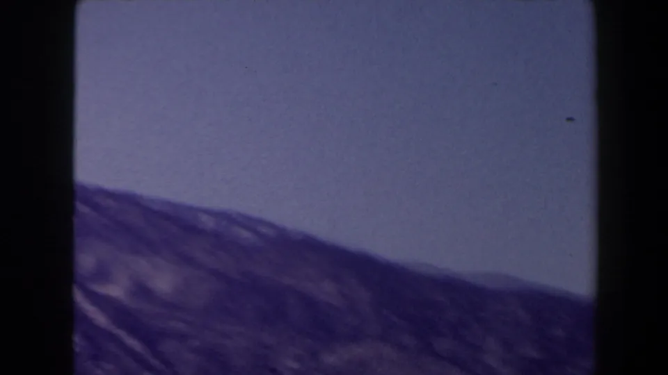 Soft 8mm frame of sloping mountain terrain and open blue sky, part of a 1958 Las Vegas-area home movie.
